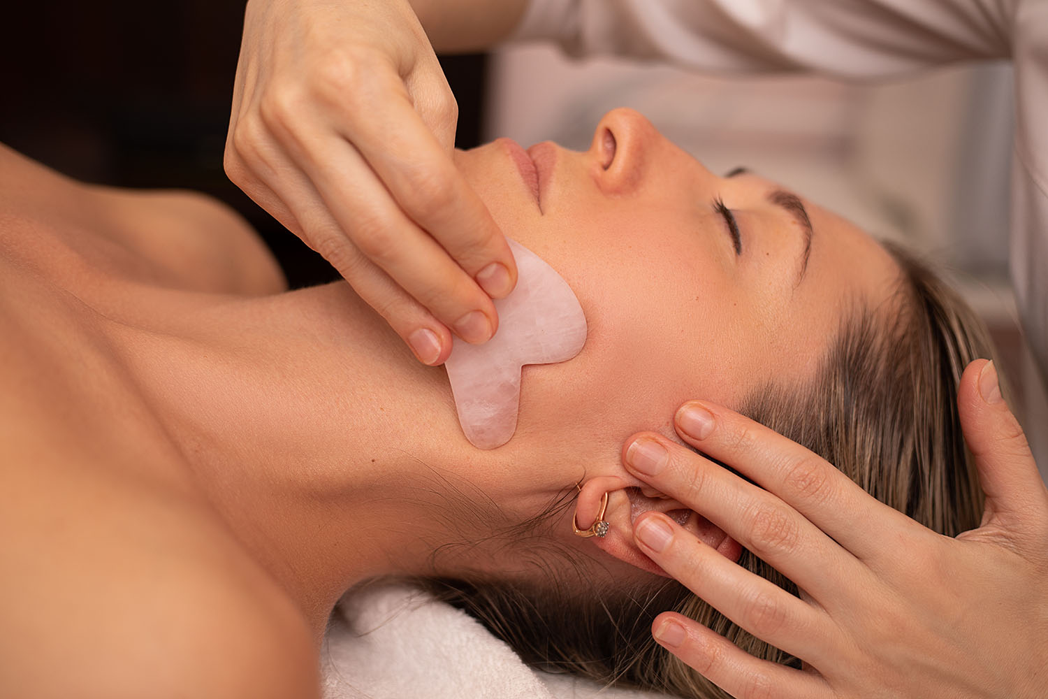Therapist gliding a rose quartz gua sha stone along a client's jawline