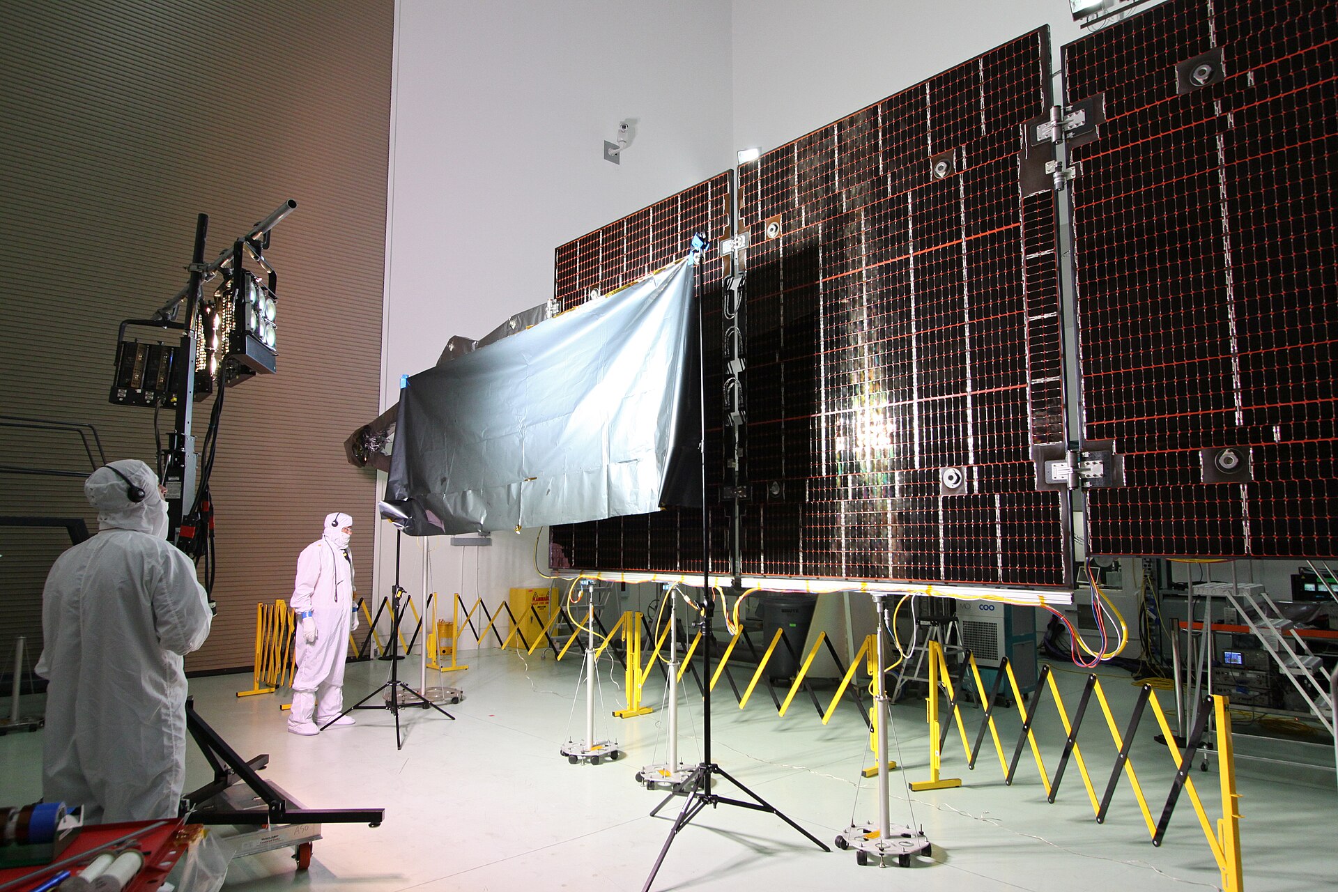 Technicians in clean-room suits inspecting a large solar array during laboratory testing