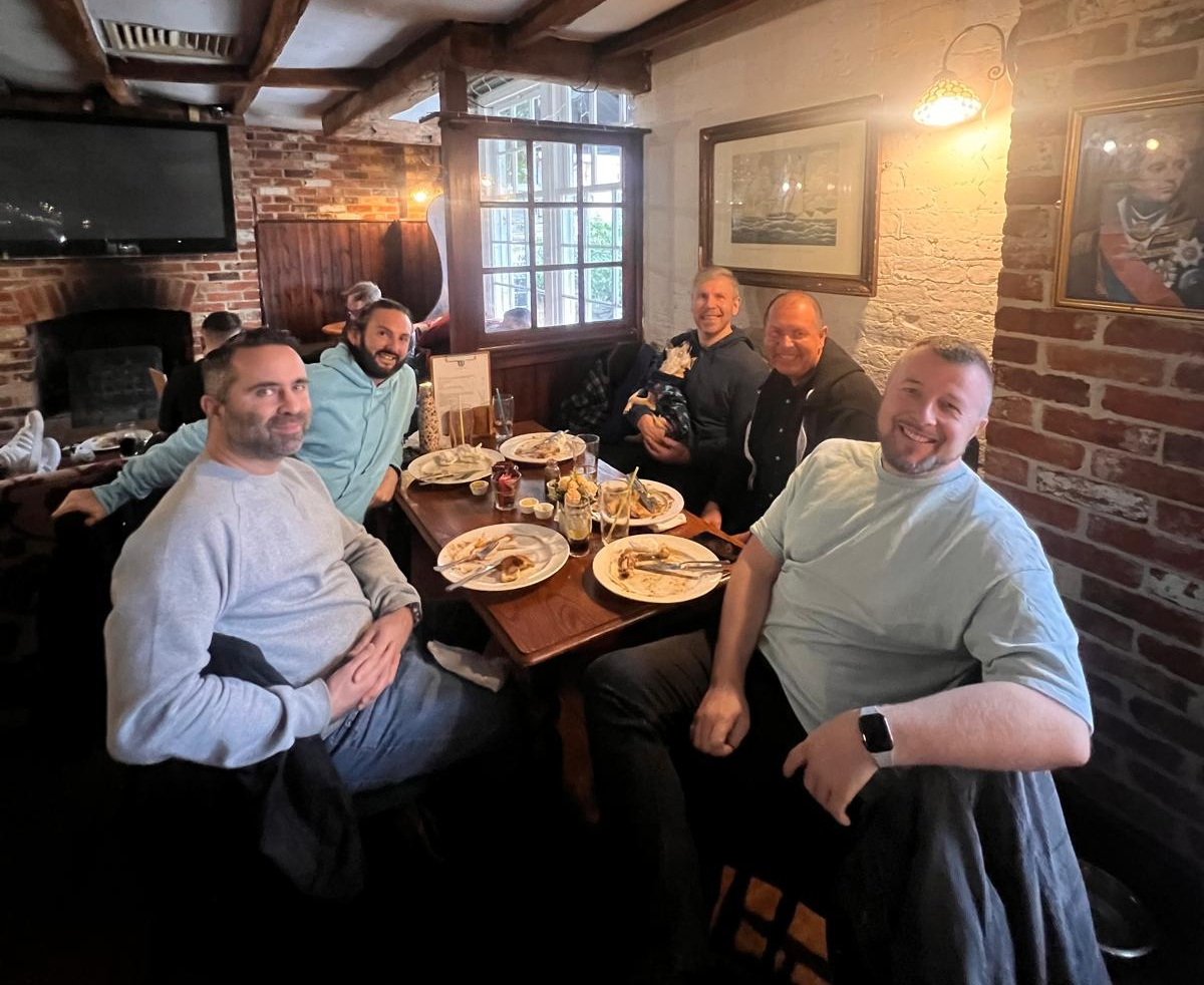 Five Tonic members smiling and sitting around a table with empty plates at The Camelford.