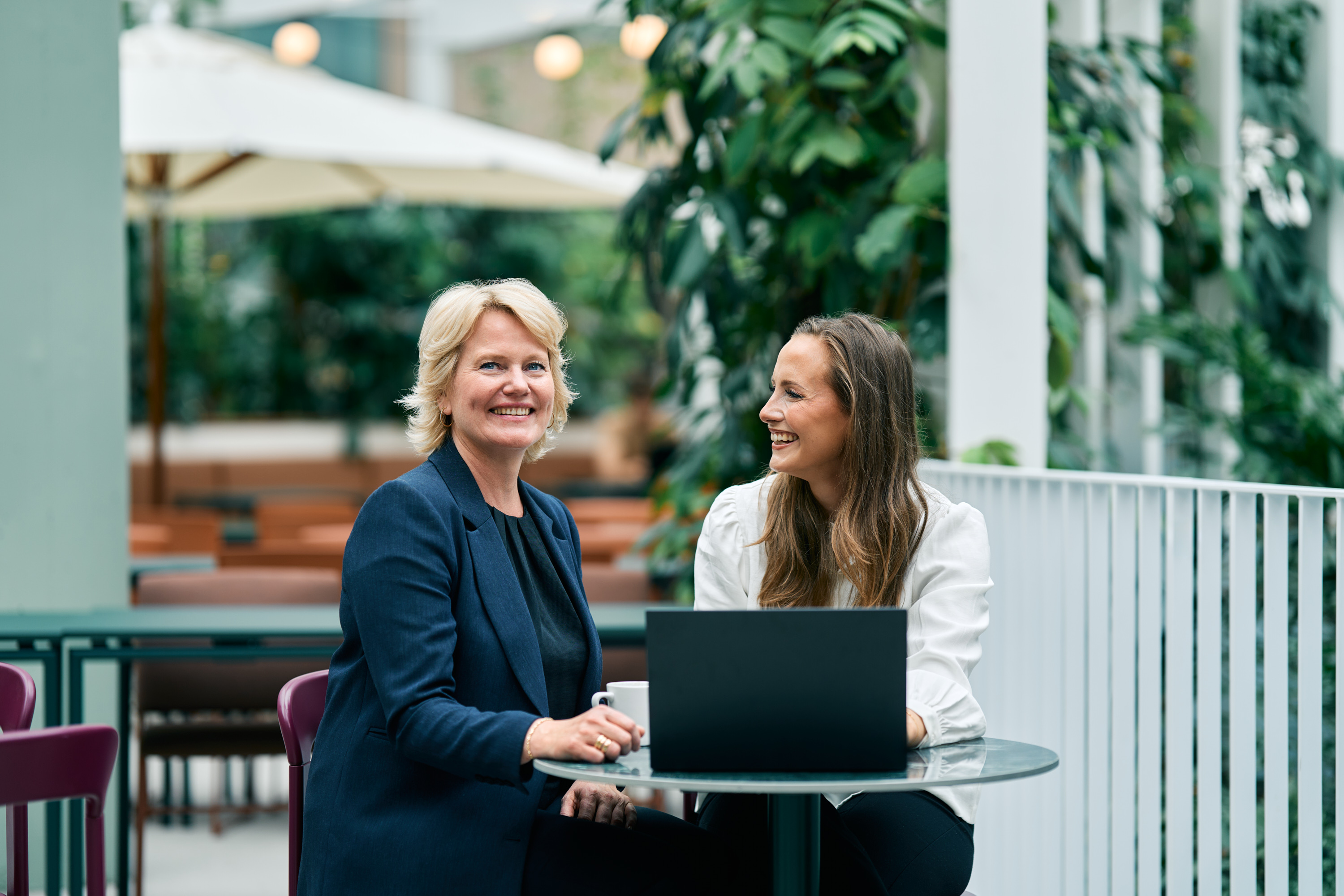 To rådgivere fra Fair Advisory ved et bord med laptop i et grønt atrium