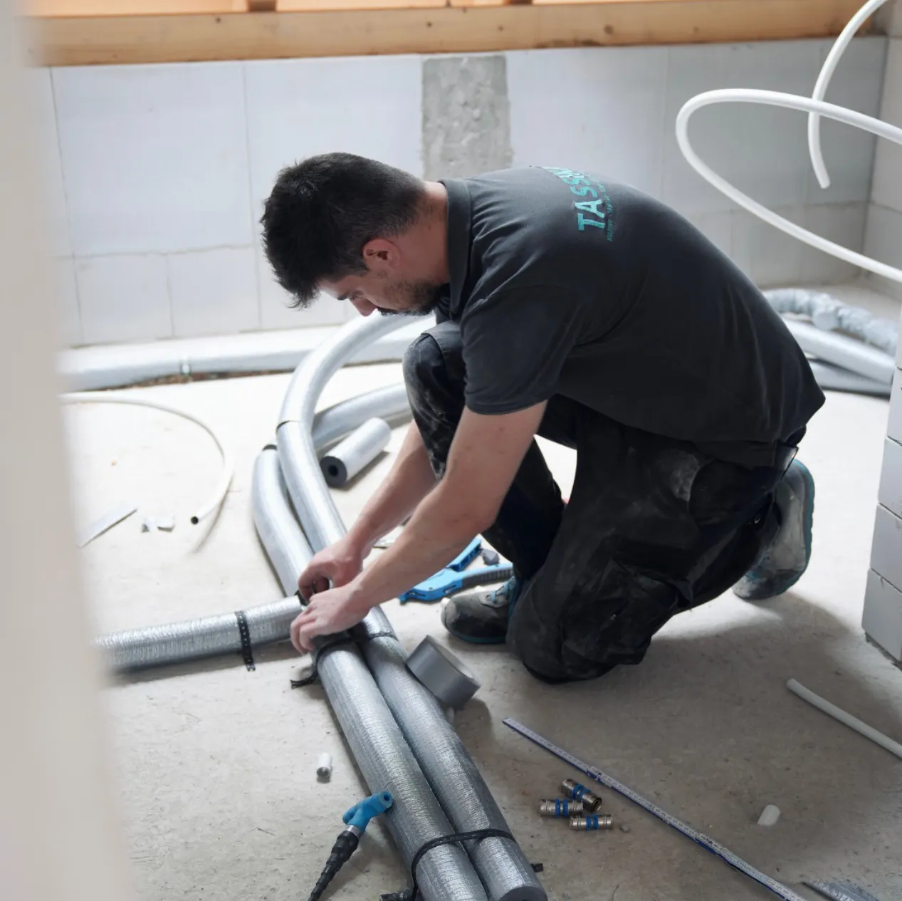 Ein Monteur von Tassikas verlegt Warmwasserrohre auf Estrich.