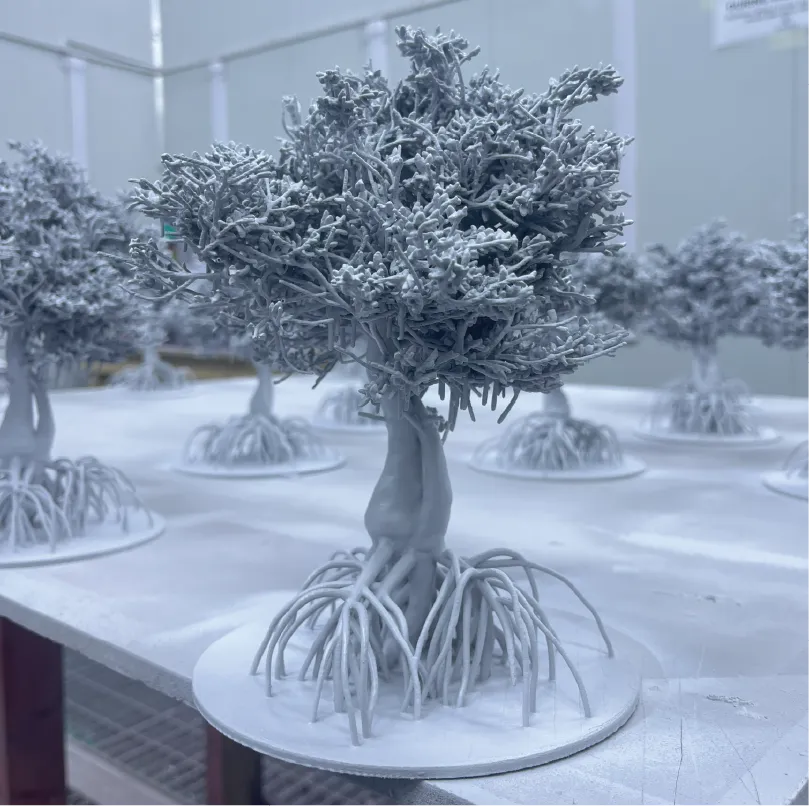 Multiple detailed gray resin 3D-printed miniature trees with exposed roots on a flat surface.