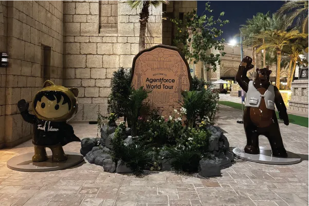 Two statues at night: a cartoon figure in a hoodie and a bear waving, flanking an Agentforce World Tour sign.