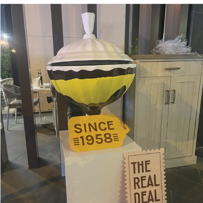 Large dessert-shaped sculpture with a yellow tag reading 'Since 1958' and a sign 'The Real Deal'.