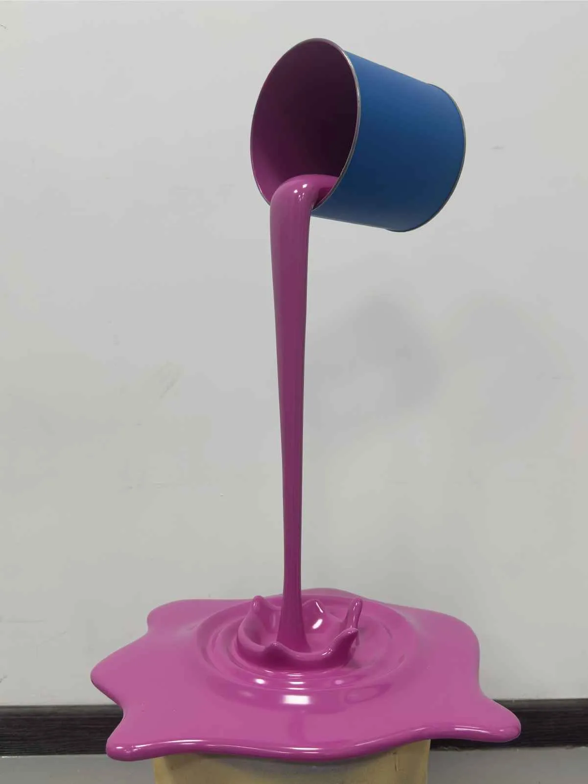 Blue bucket pouring thick purple liquid onto a surface forming a splash shape sculpture.