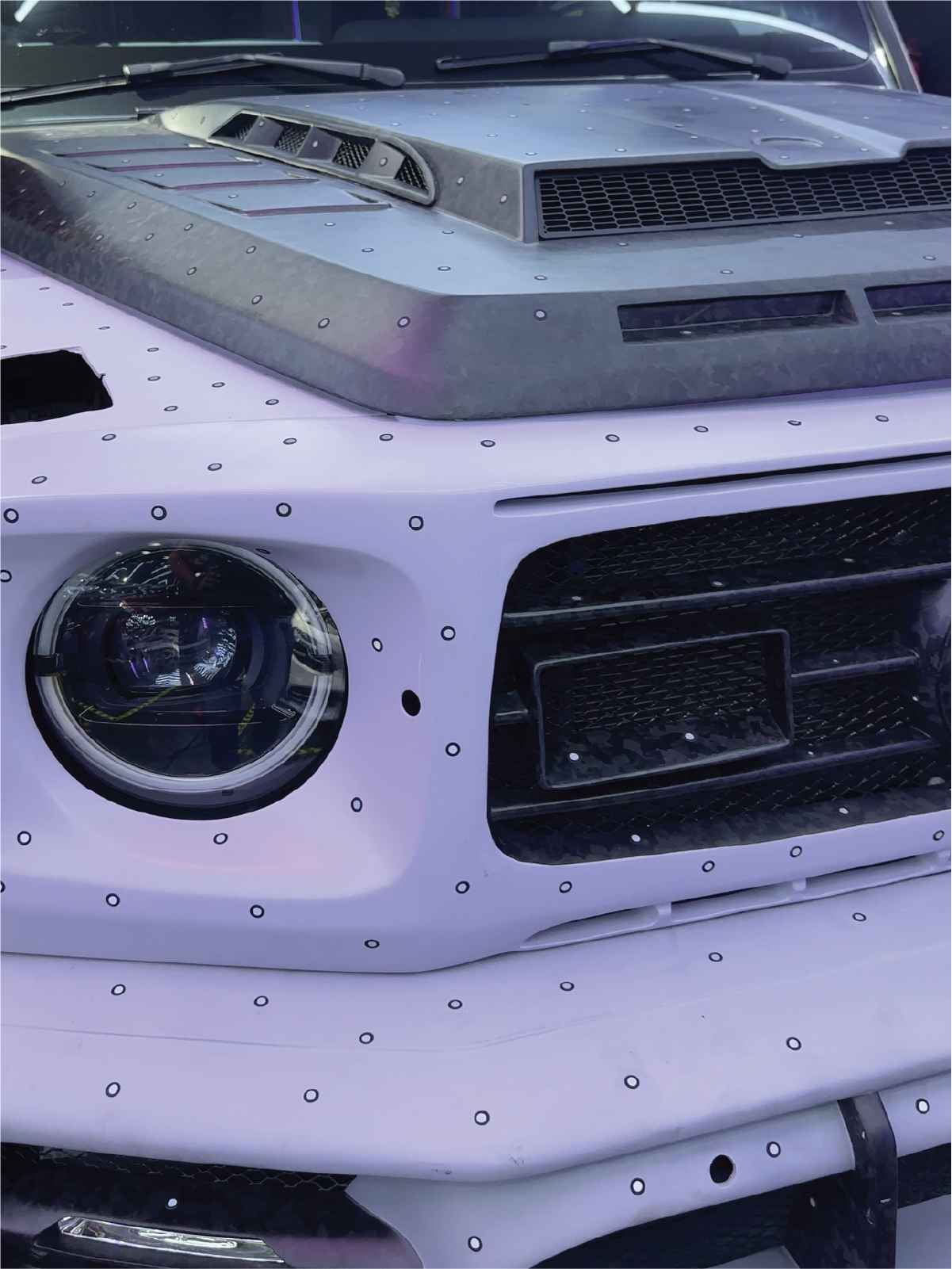 Close-up of a white car front with round headlight and black ventilation grilles on the hood and bumper.
