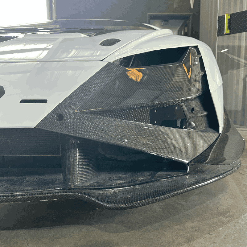 Close-up of a car's front corner showing a white body with black carbon fiber aerodynamic parts.