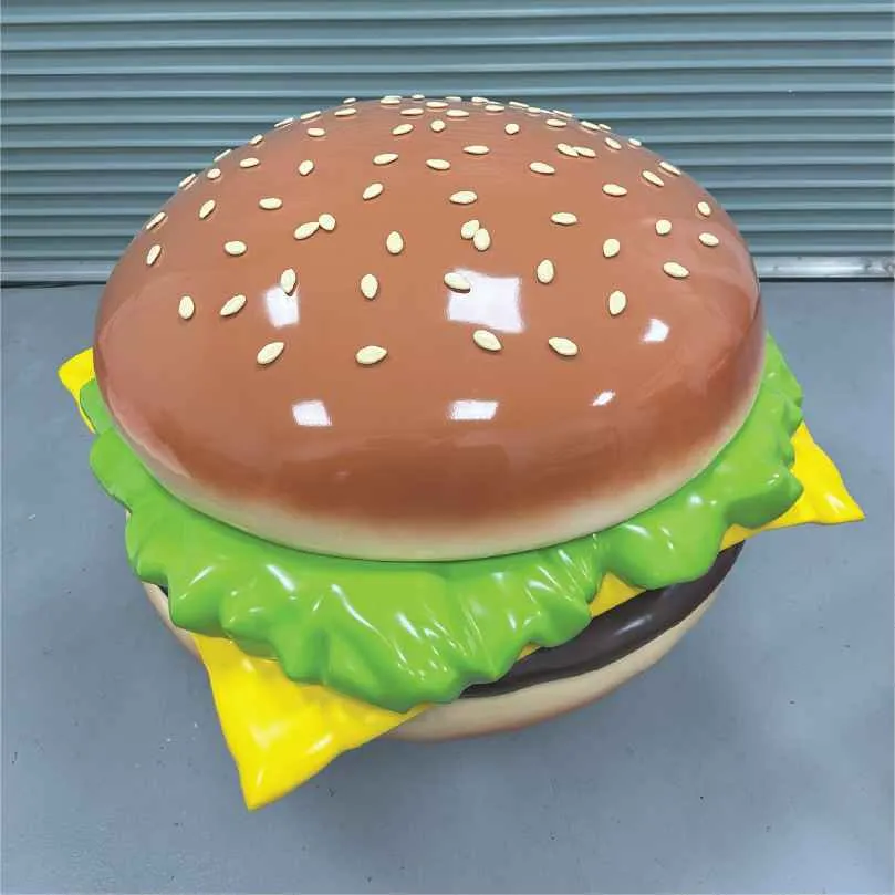 Large, shiny hamburger sculpture with lettuce, cheese, and sesame seeds on bun.