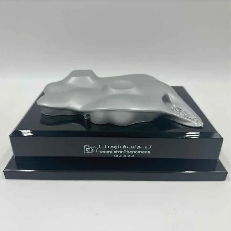 Silver abstract sculpture on black base labeled teamLab Phenomena Abu Dhabi.