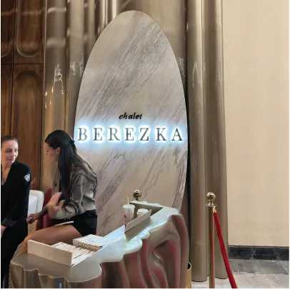Two women sitting by a marble sign reading 'chalet BEREZKA' inside a building with polished walls.