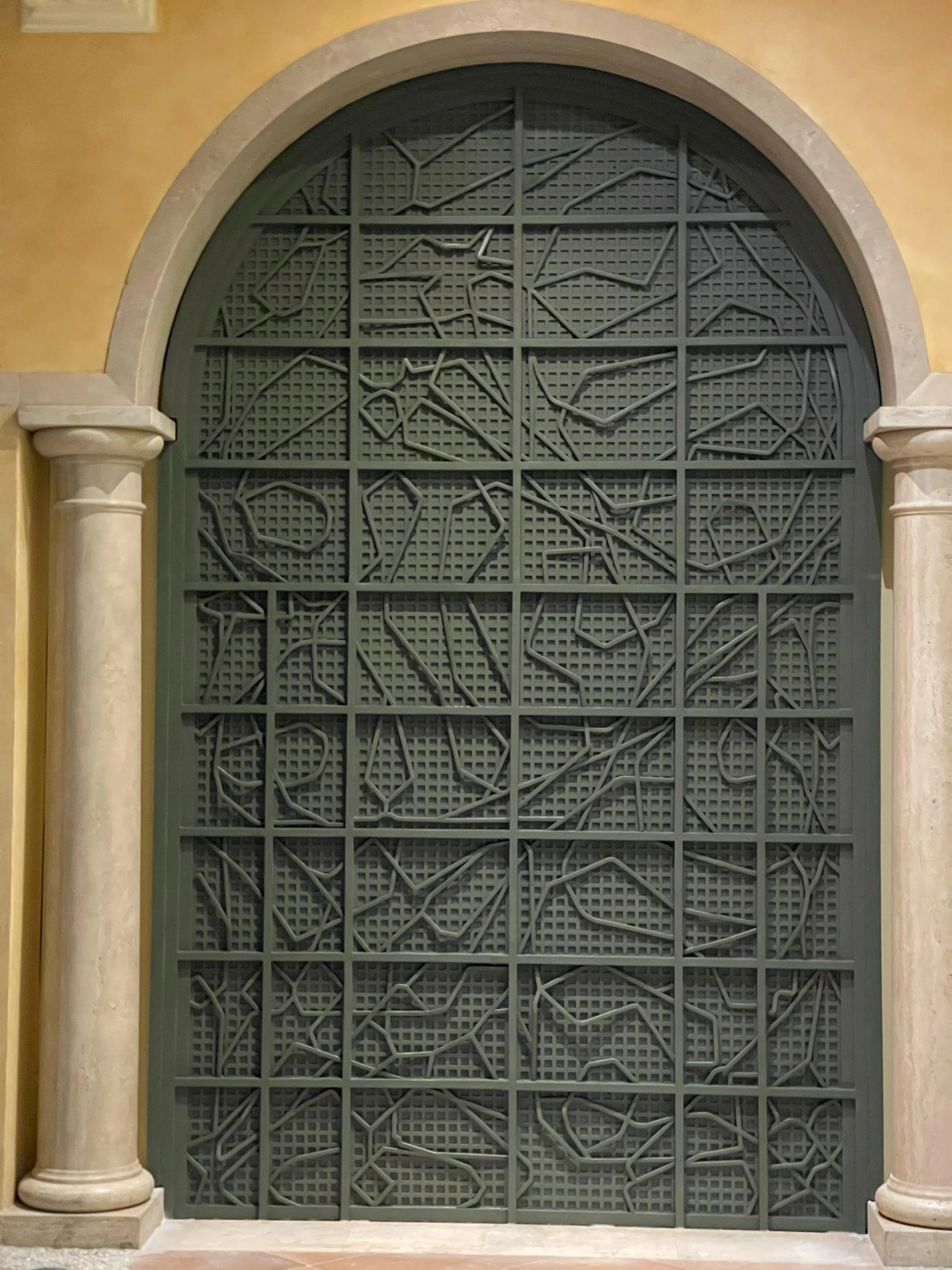 Large arched decorative metal gate with abstract geometric patterns, framed by two stone columns.