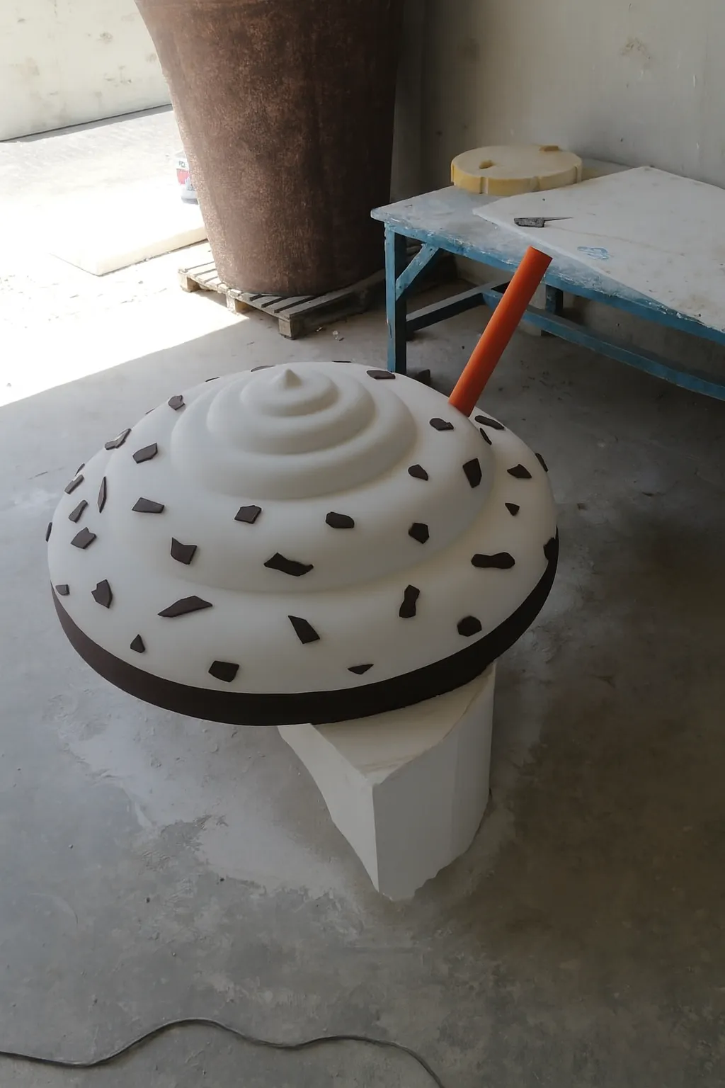 Large foam model resembling vanilla ice cream with chocolate chips and an orange straw on a block.