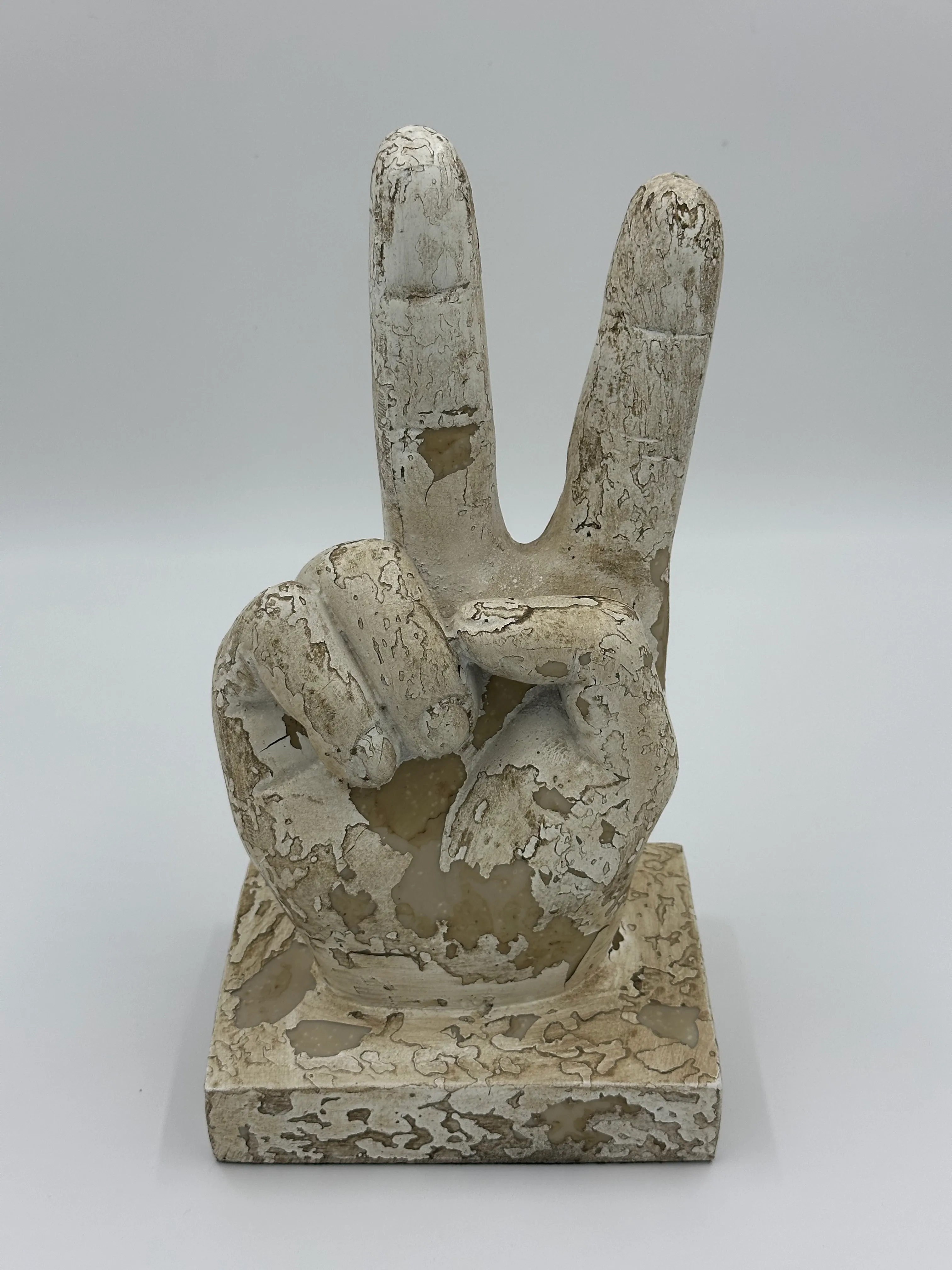 Weathered sculpture of a hand making a peace sign with two fingers raised on a square base.