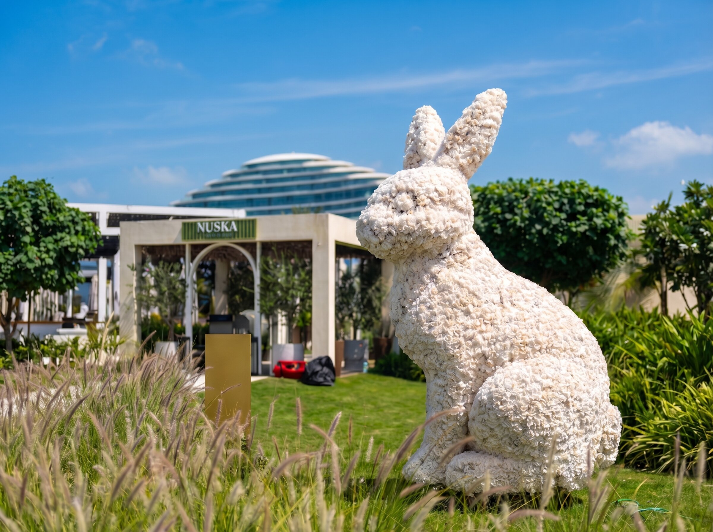 Large white rabbit sculpture made of flowers on green grass near a garden cafe under a blue sky.