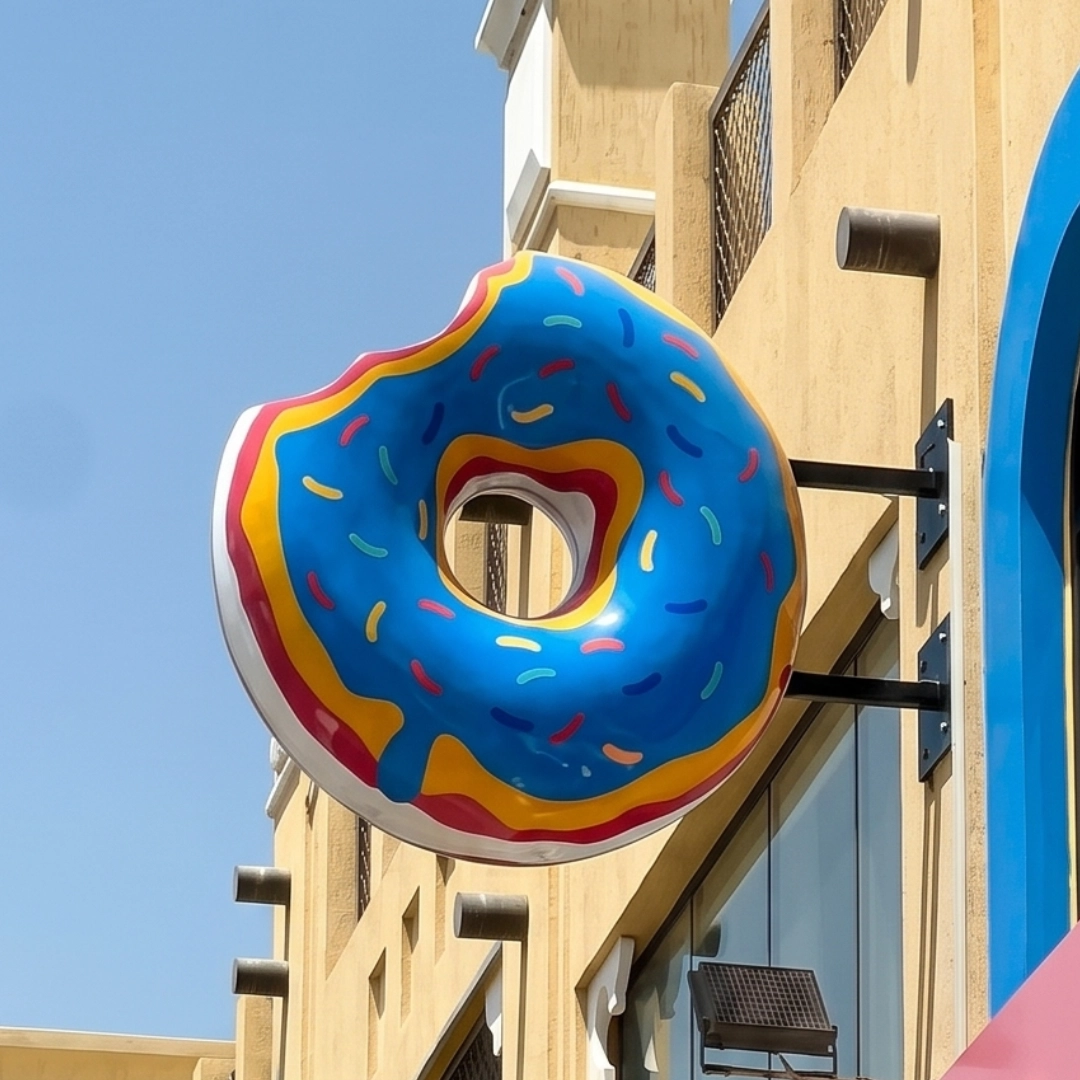 Large colorful donut sign with blue frosting and sprinkles mounted on a building exterior.