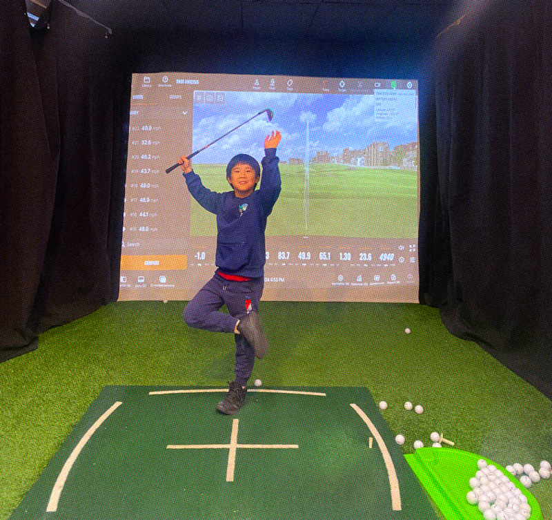 Student smiling in front of a golf simulator