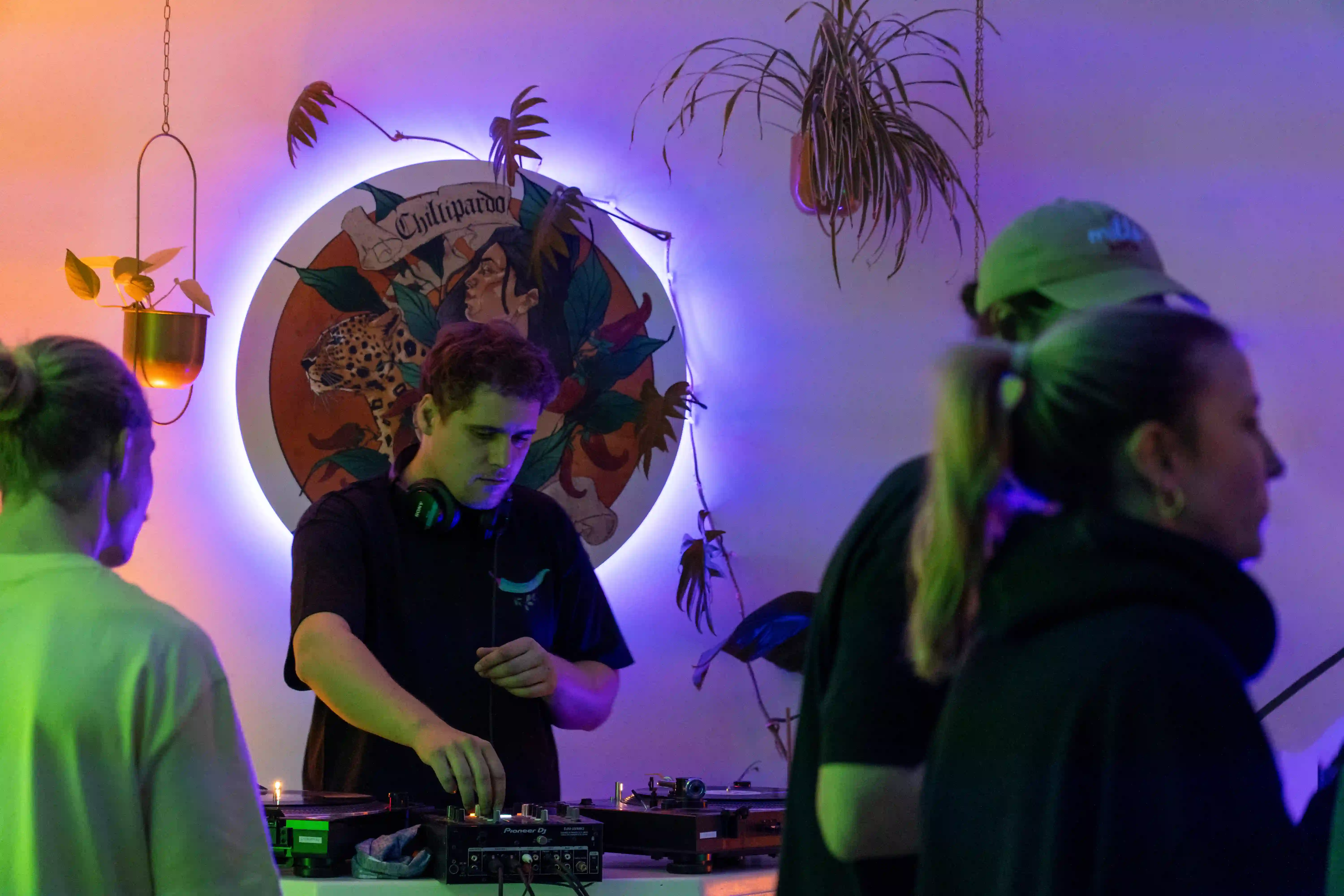 Five colorful shot glasses with different liquids lined up on a table with hand-drawn cocktail glass illustrations and a Pixar-themed flyer.