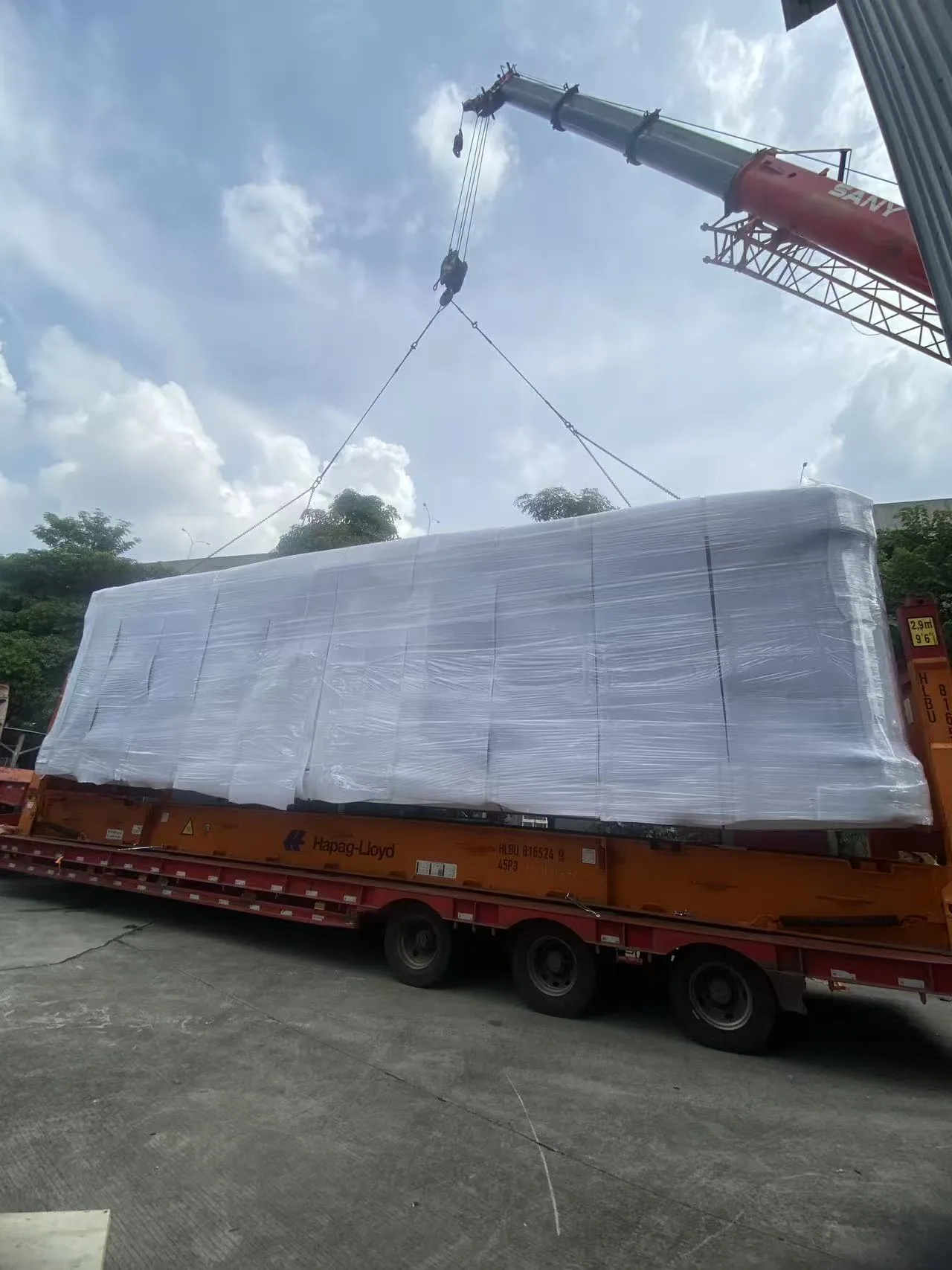 Crane lifting a wrapped capsule home off the trailer on site