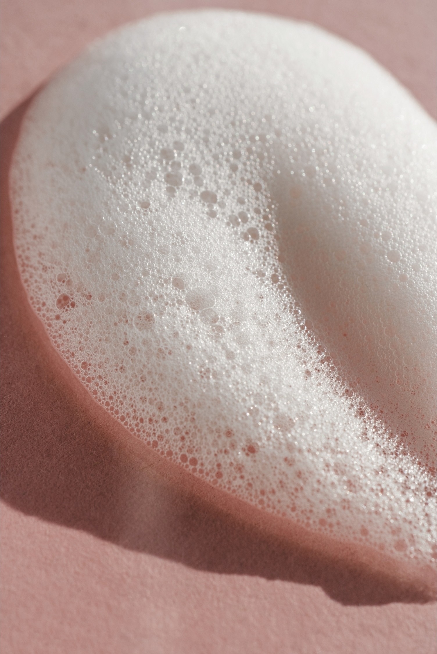Close-up of white soap suds with bubbles on soft pink background