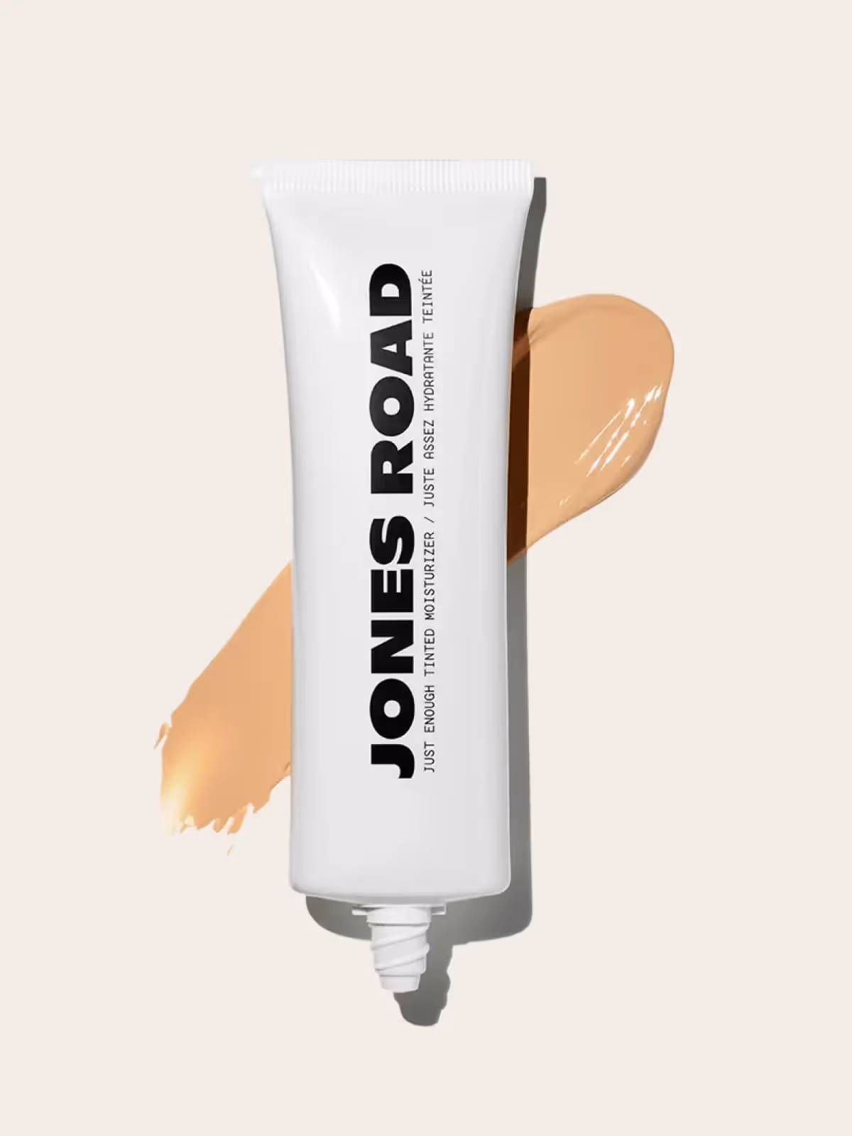 Jones Road tinted moisturizer tube with makeup swatch on light background