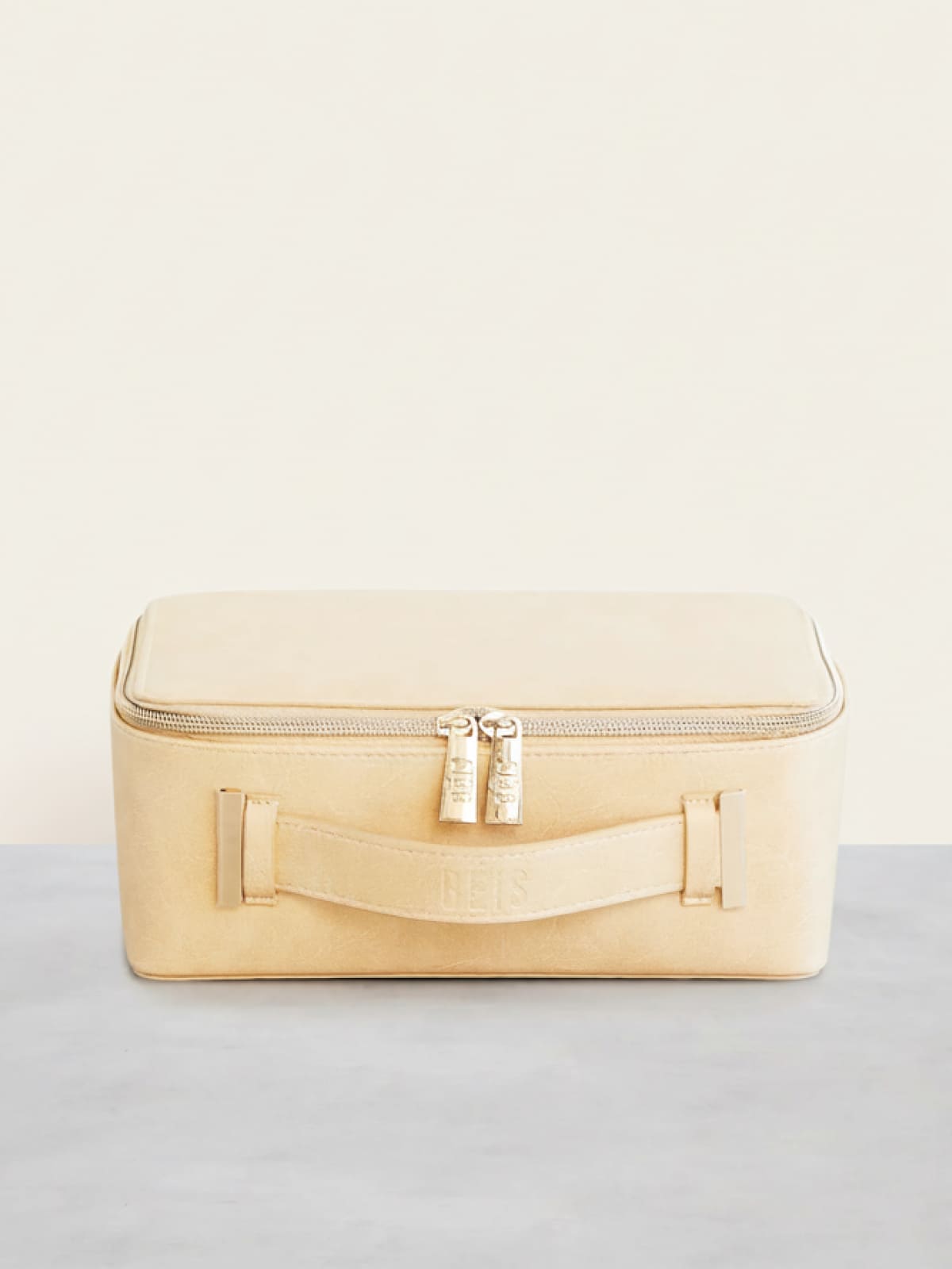 Cream-colored travel case with zipper and handle on neutral background