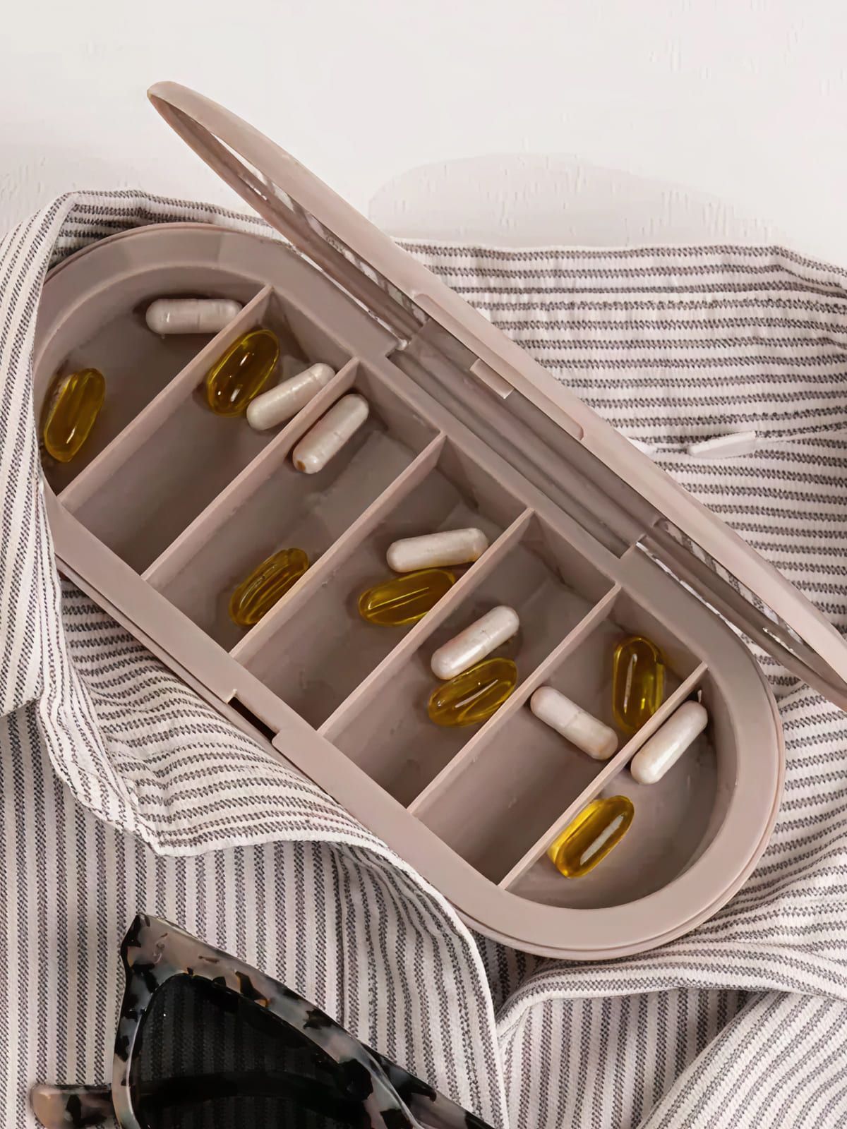 Pill organizer with yellow and white capsules on striped fabric