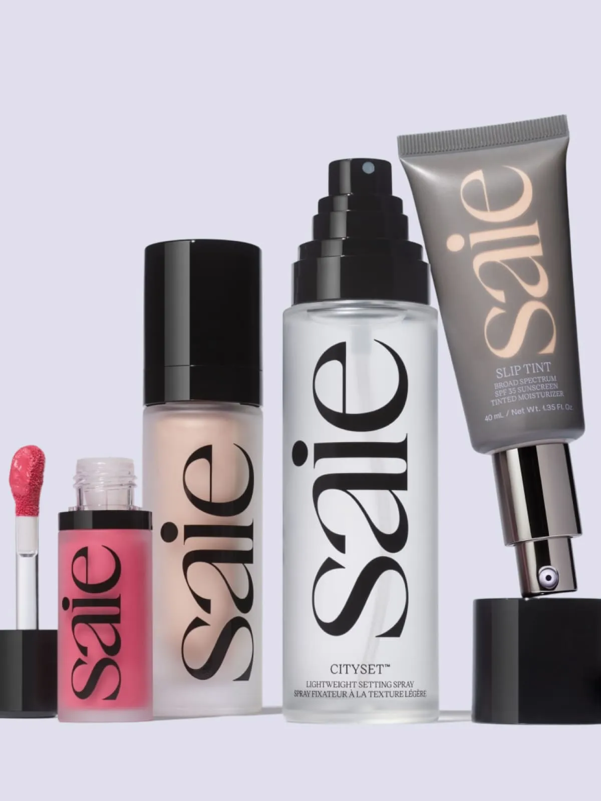Saie cosmetics collection including pink lip gloss, foundation, setting spray, and tinted moisturizer.