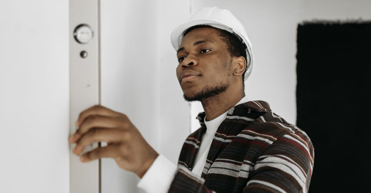 A construction worker wearing a hard hat accurately measures with a level indoors.