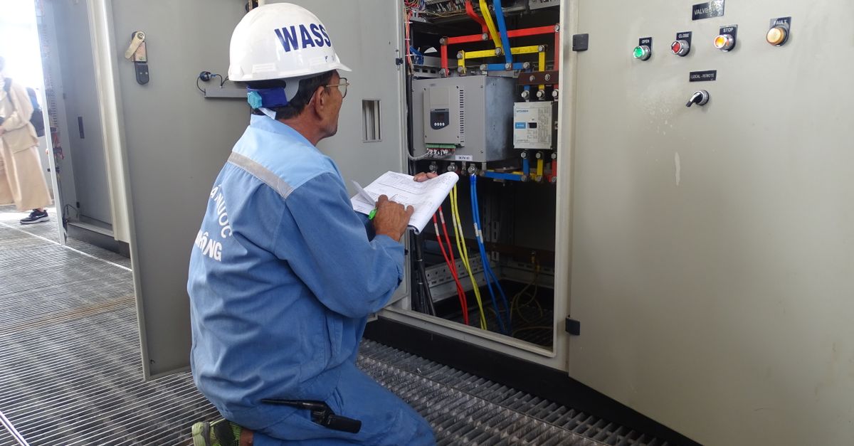 Engineer in uniform inspecting an electrical control panel in an industrial setting.