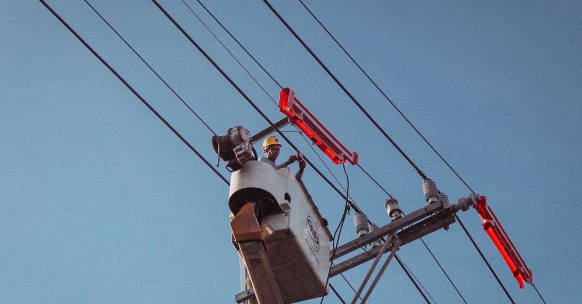 Electrician in a lift repairing overhead power lines on a clear day.