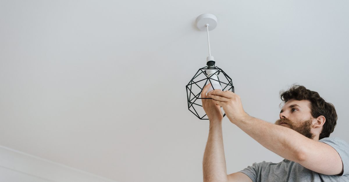 From below of male screwing light bulb into new fashionable lamp during renovation work in apartment