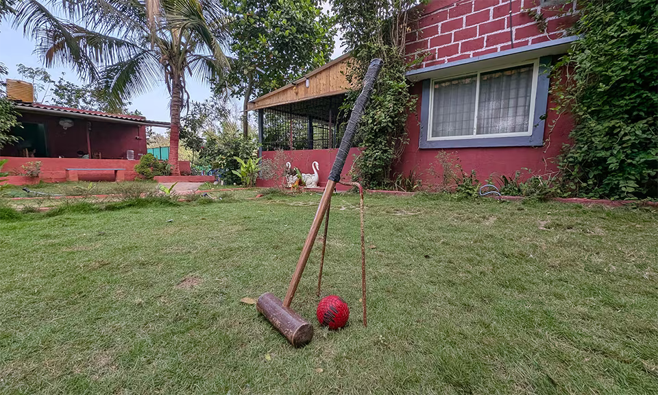 Outdoor croquet game setup at Major's Retreat with mallets and a red ball on lush green grass, featuring a red brick building and trees in the background.