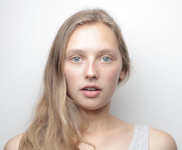 Young woman with long blonde hair and blue eyes looking directly at the camera against a white background.