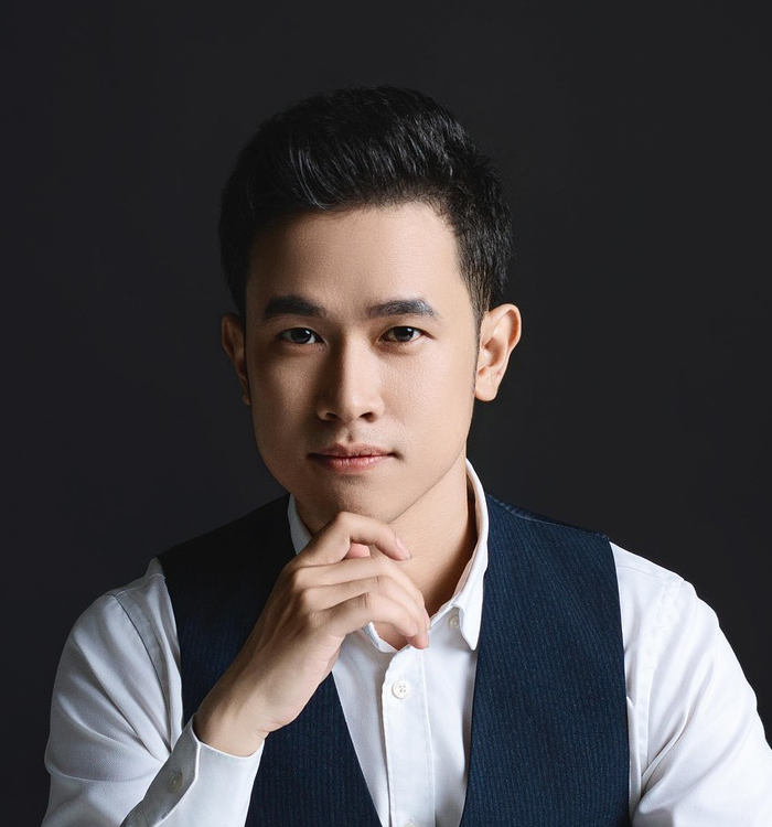 Portrait of a young man wearing a white shirt and dark vest, posing thoughtfully against a dark background.