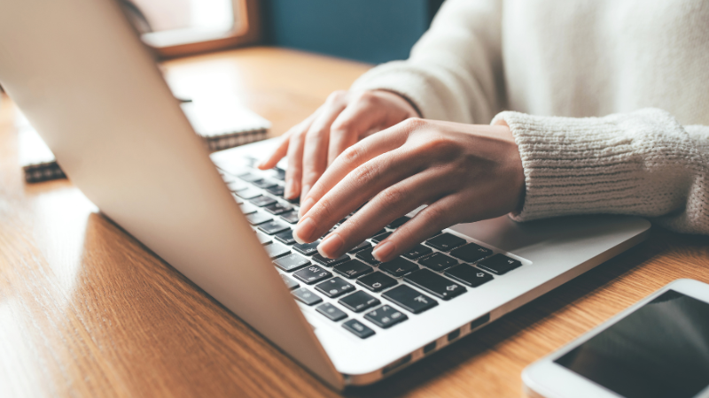 hands with white sweater sleeves typing on a computer