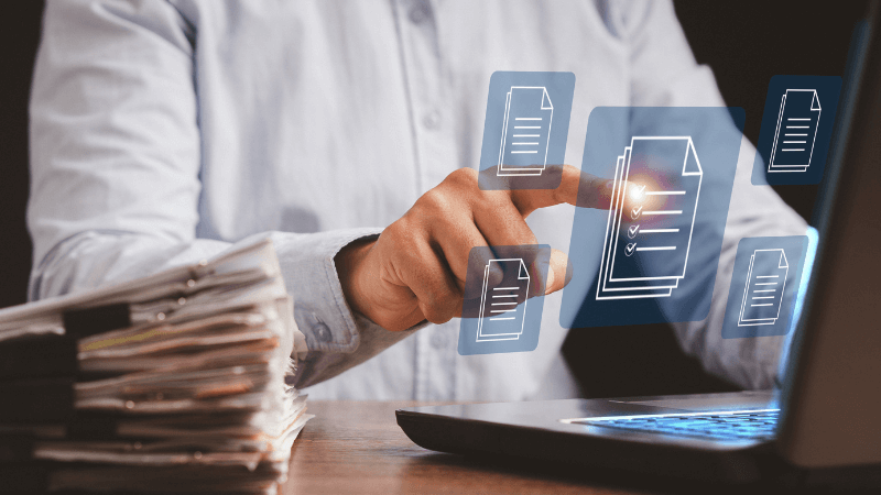 stack of documents with a laptop showing digital documents 