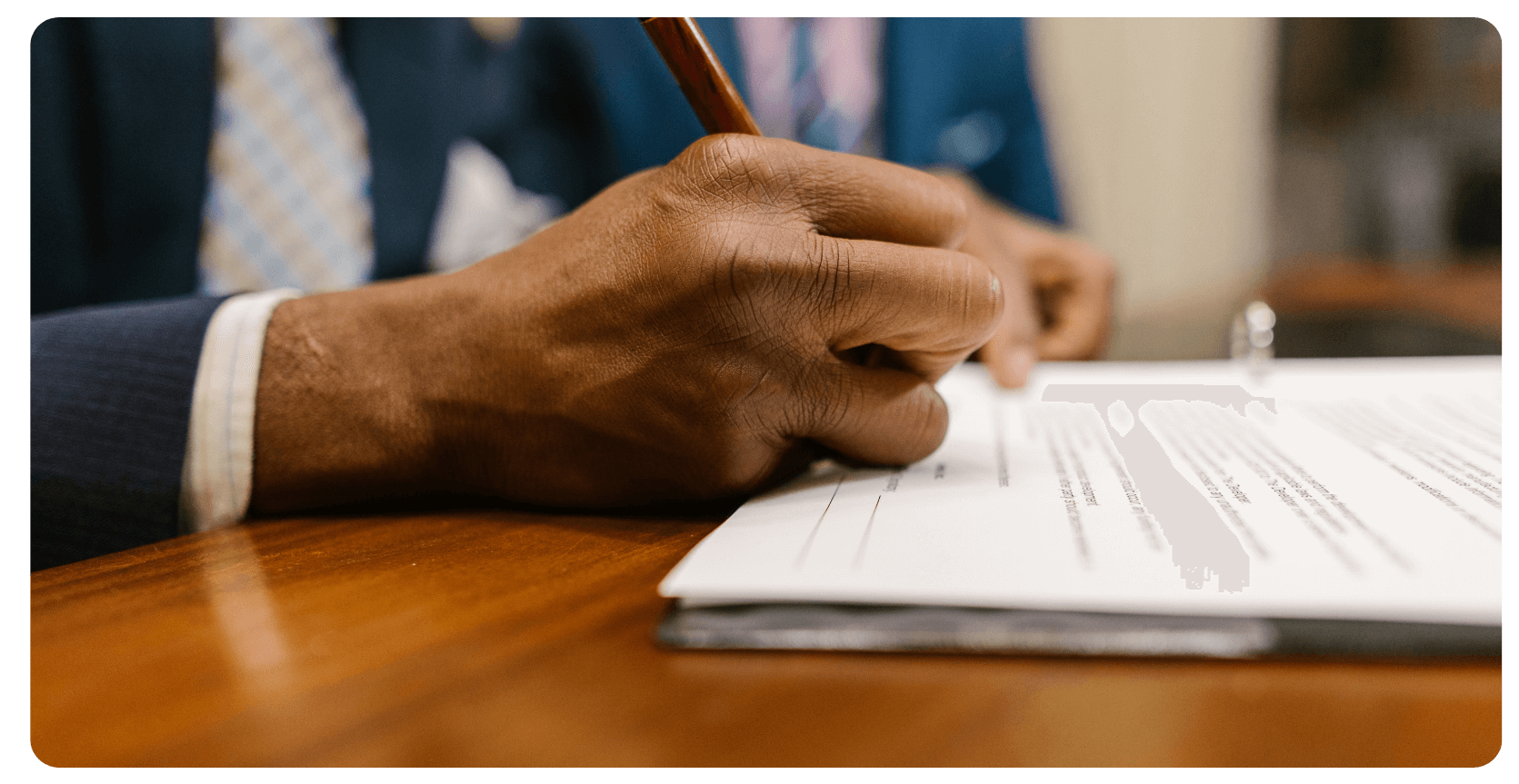 black man in suit signing a document with a red pen