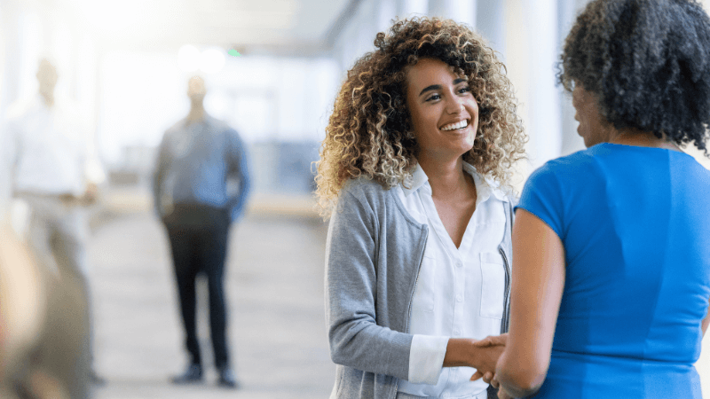 two black women in business clothes shaking hands in an office