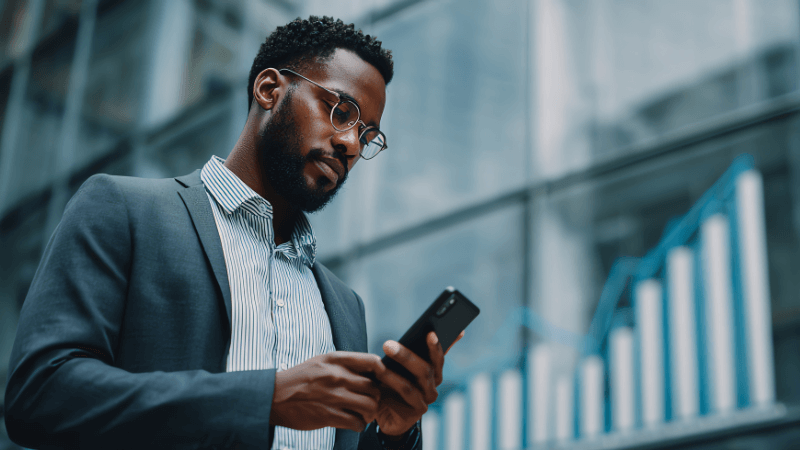 black man using phone with bar graph behind him in front of an office building