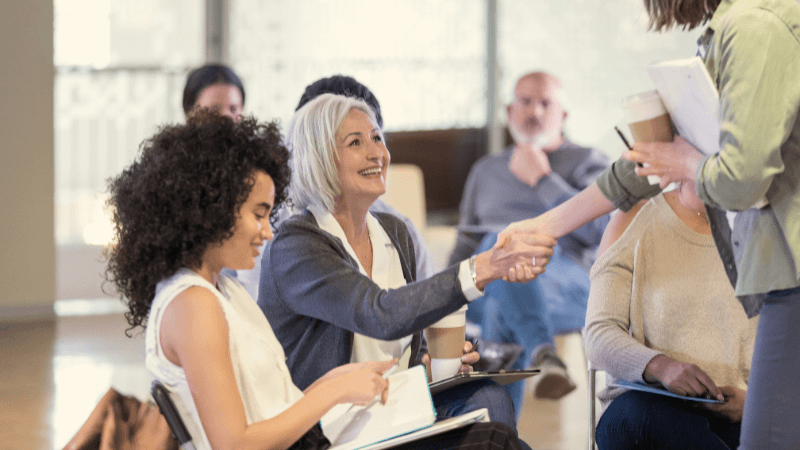 older white woman shaking hands at a group meeting