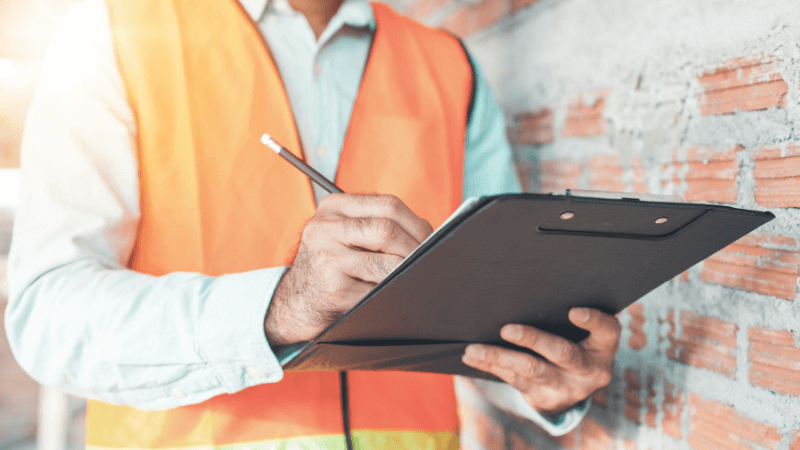 an inspector with a clipboard in front of a brick wall
