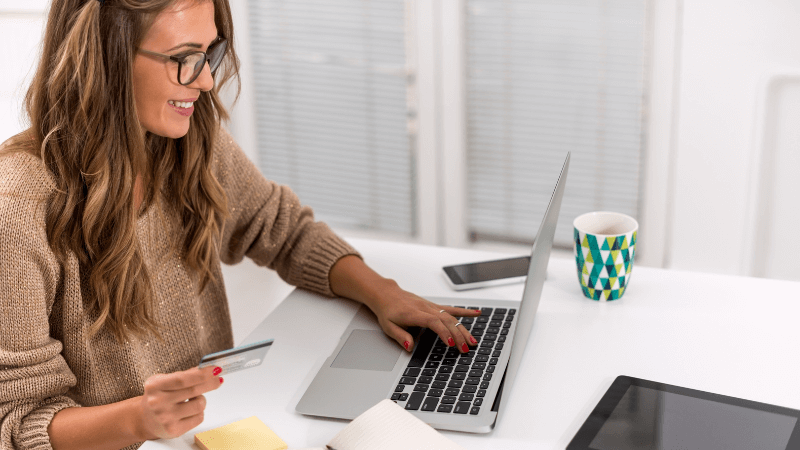white lady with brown hair sitting a table with a credit card paying online