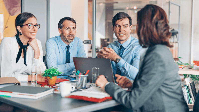 four men & women sitting around a table in an office having a discussion