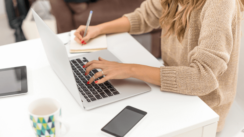 woman with blonde hair in beige sweater working on a laptop 