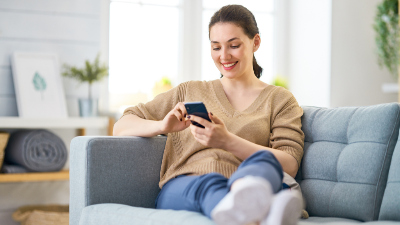 Woman seated on her couch at home, scrolling through her smartphone