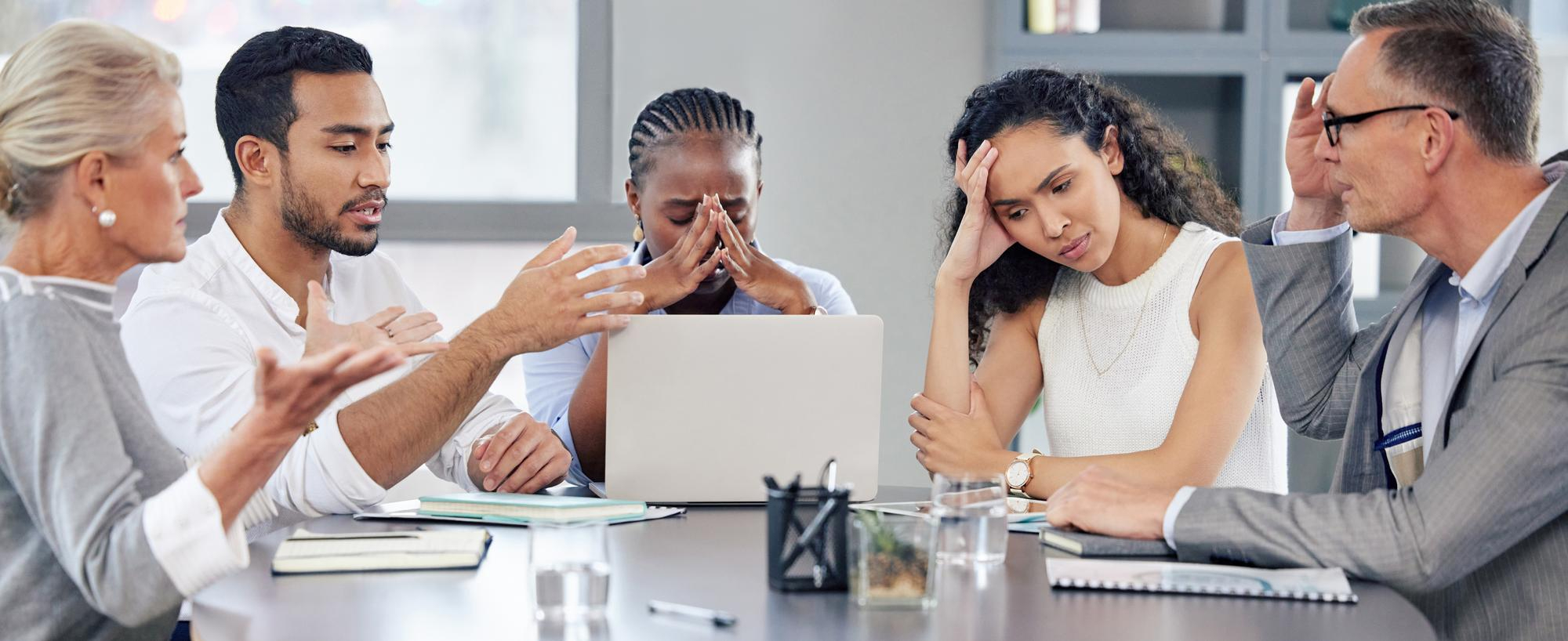 A group of people sitting around a table in a conference room looking stressed