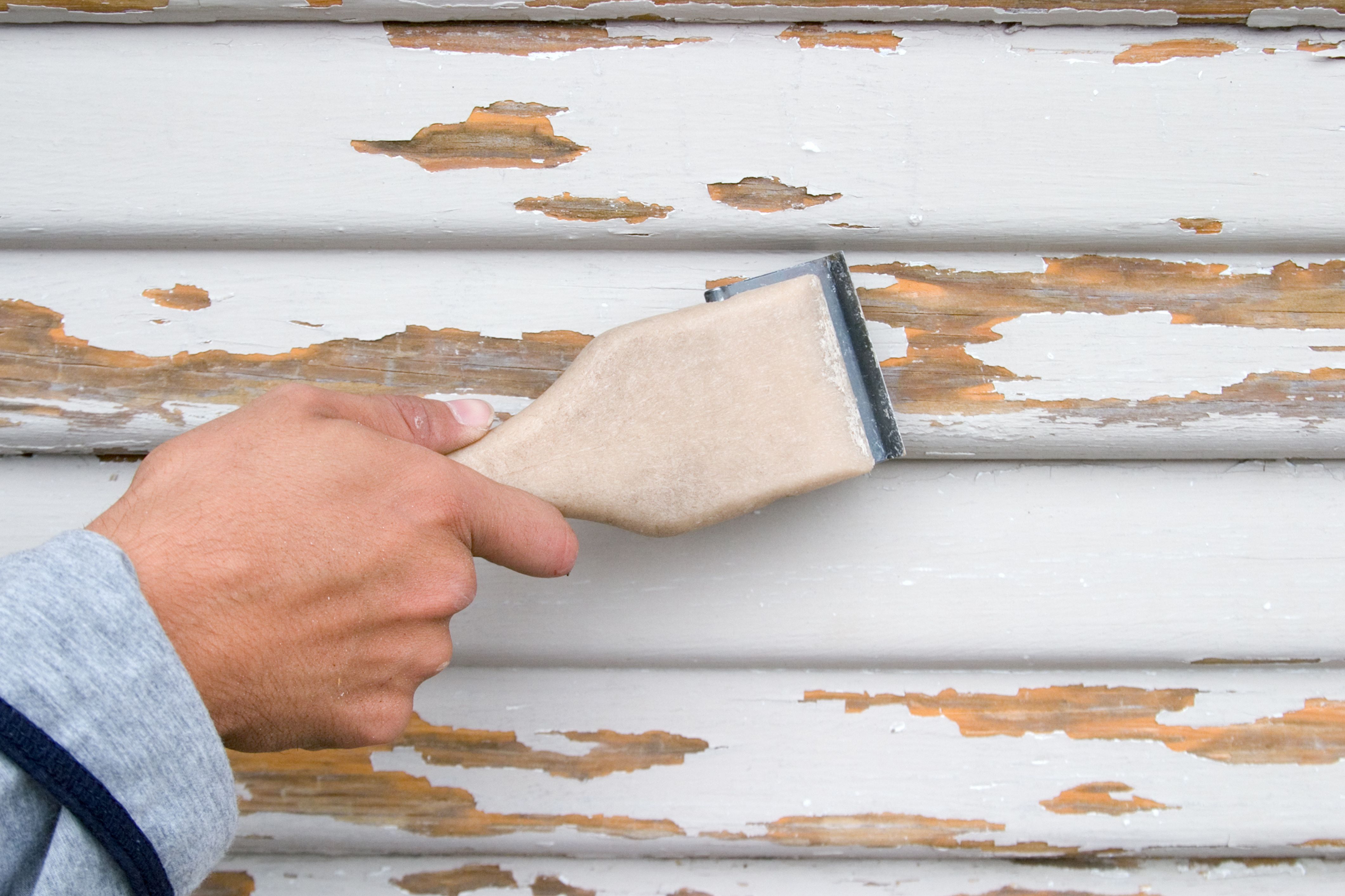A person preps a surface of a house in their HOA community for painting.