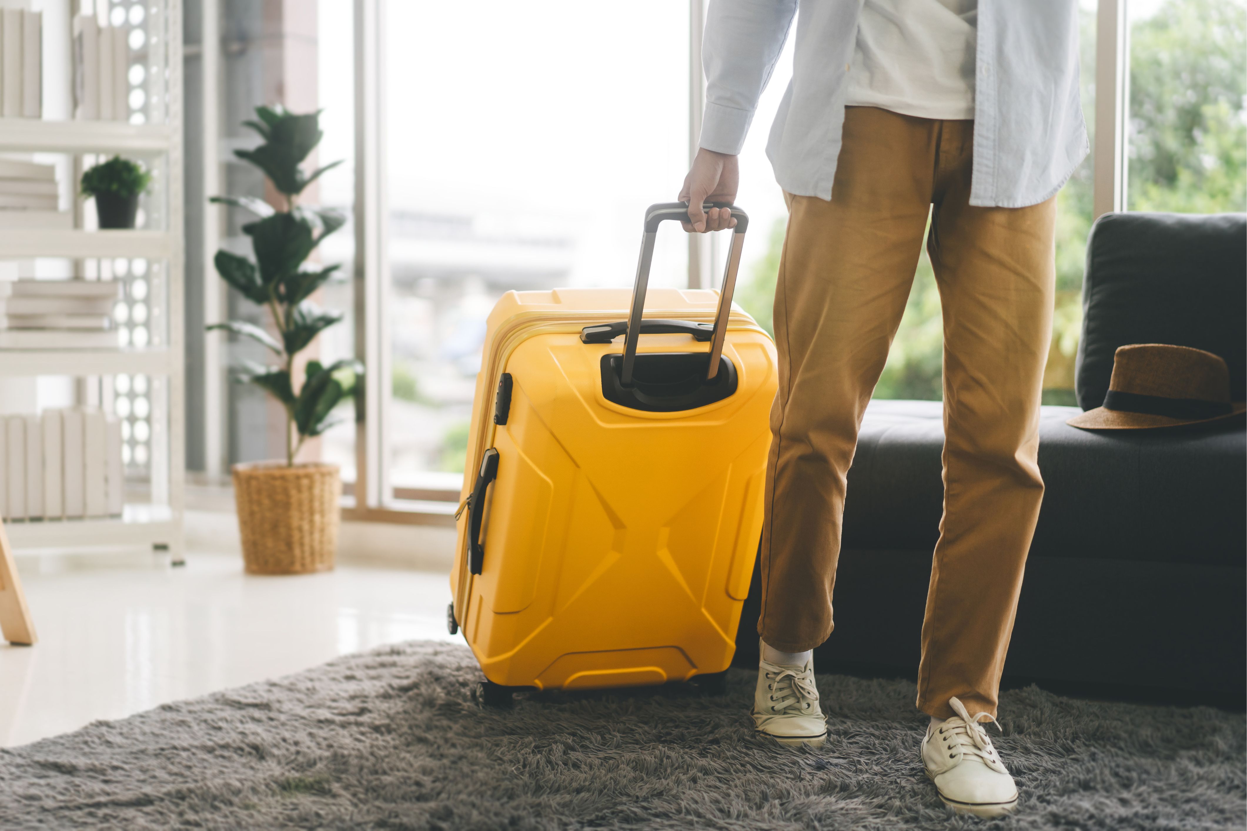 A person wheels a yellow suitcase out of their house, ready to follow an organized holiday travel plan.