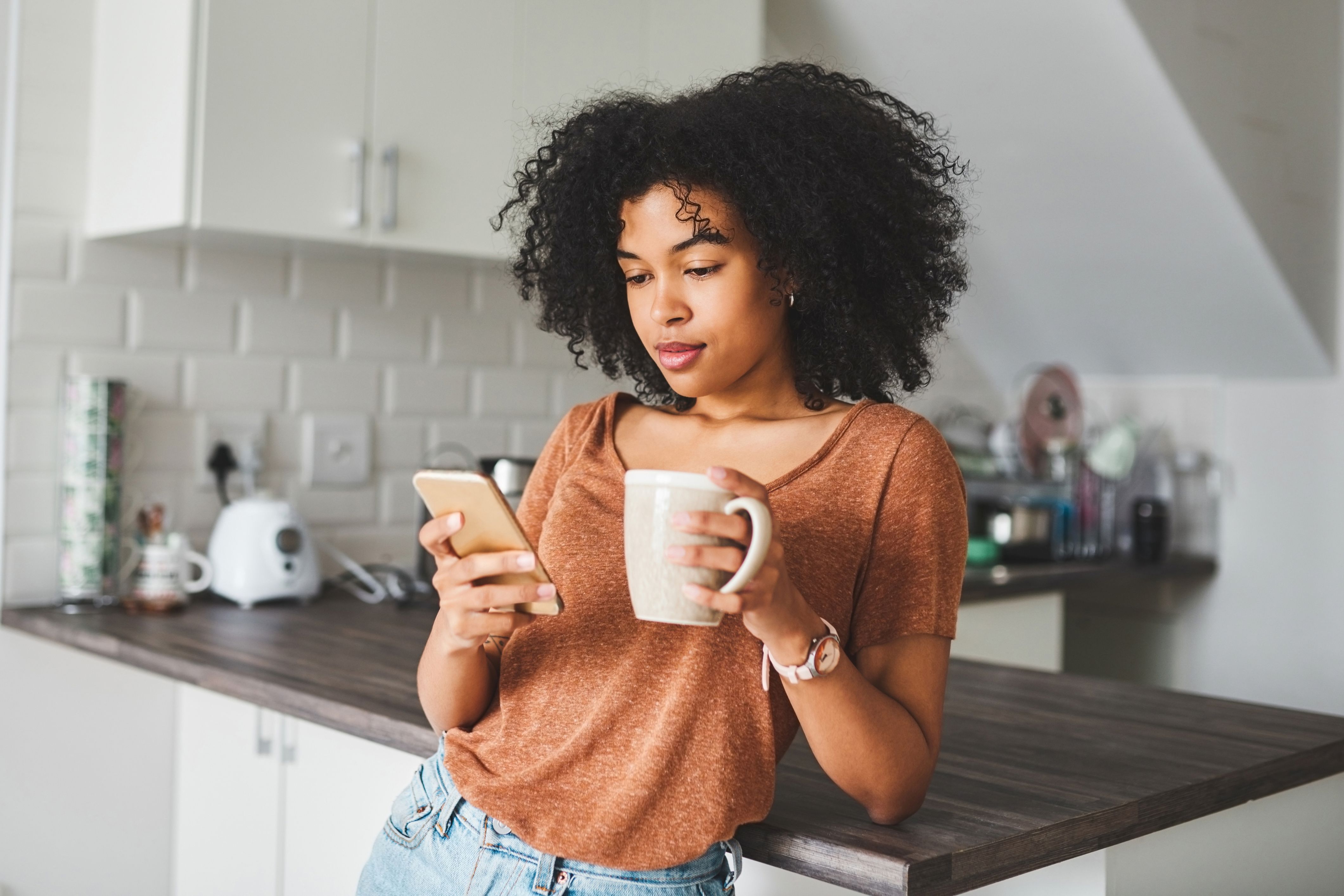 An HOA manager stands in her kitchen checking her phone for community updates.