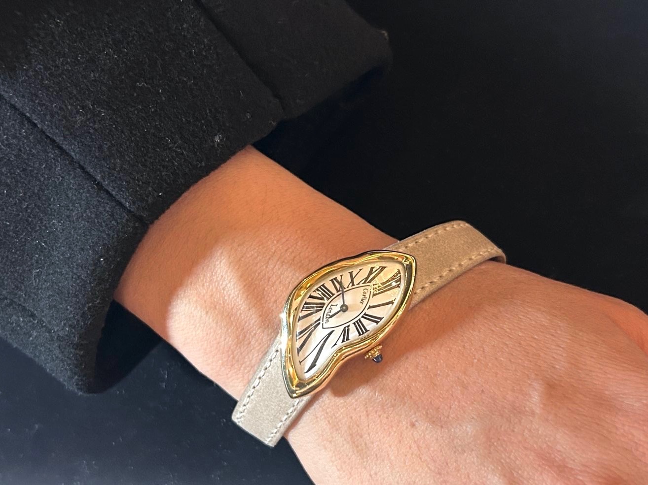 A woman wearing a Cartier 'London Crash' wristwatch with a beige strap.